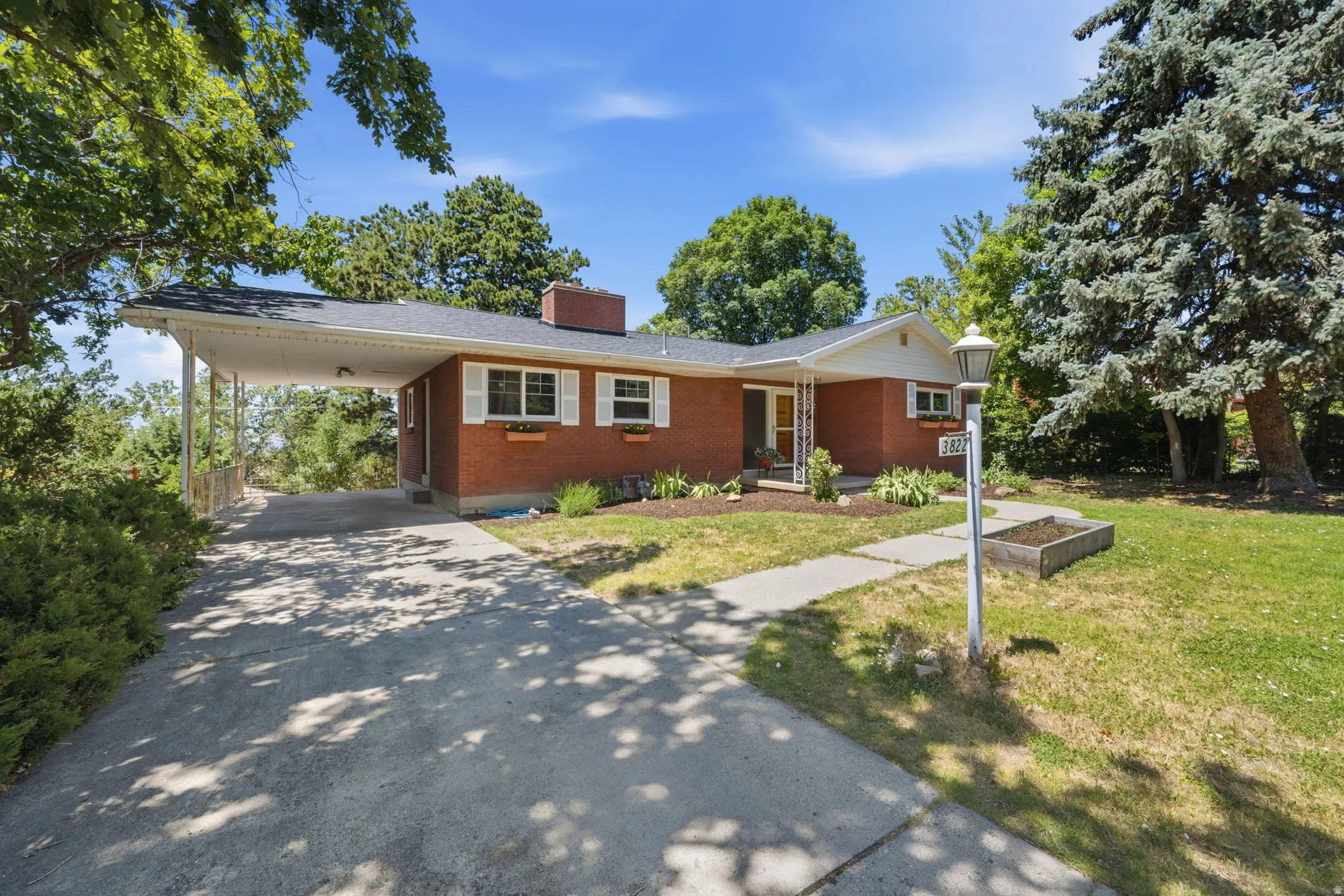 Brick exterior residence featuring a covered carport, established landscaping, and a concrete pathway leading to the front entry