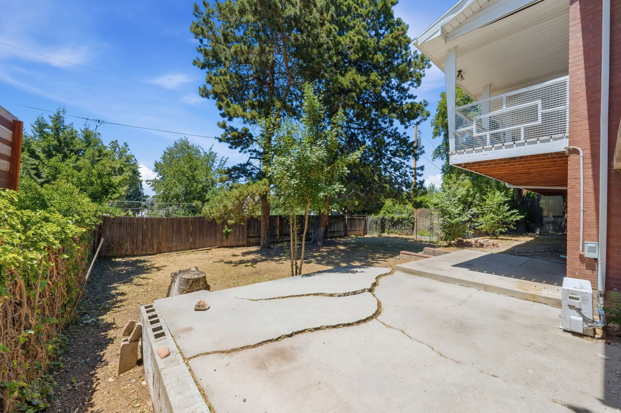 Expansive backyard with a concrete patio, mature trees, and privacy fencing