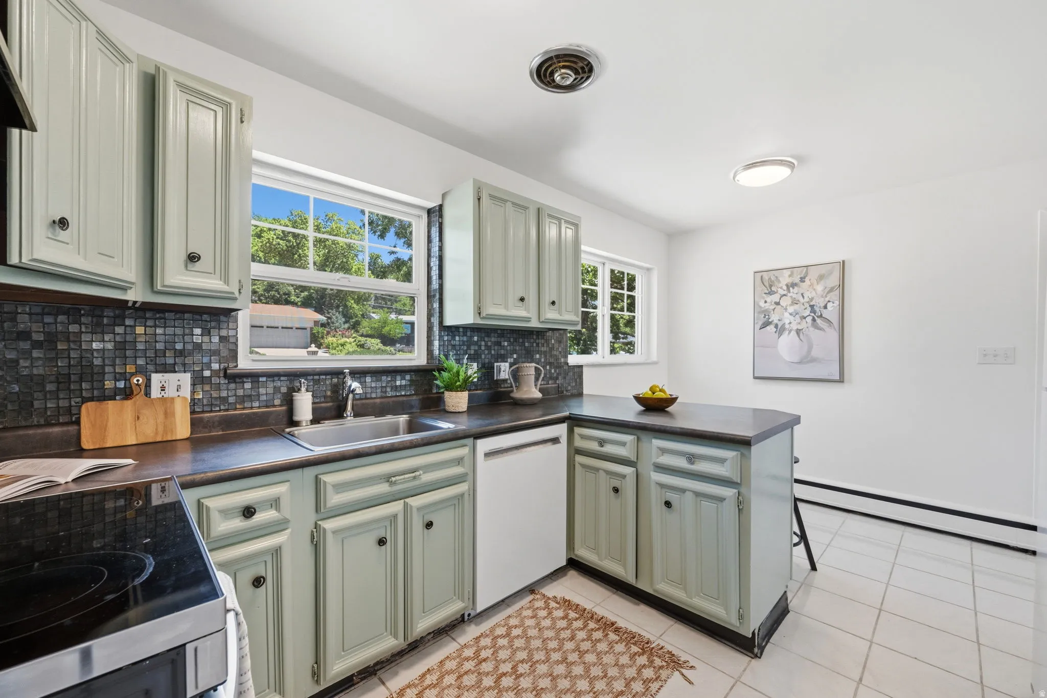 Kitchen featuring light green cabinetry, dark countertops, and a mosaic tile backsplash