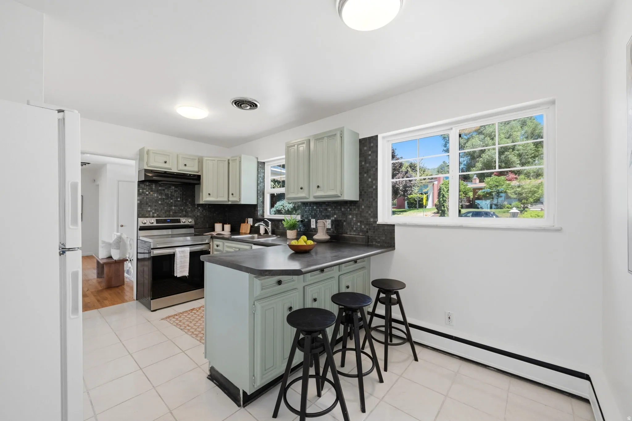 Kitchen featuring light-colored cabinetry with dark hardware, dark stone-finish countertops, and a full-height dark backsplash