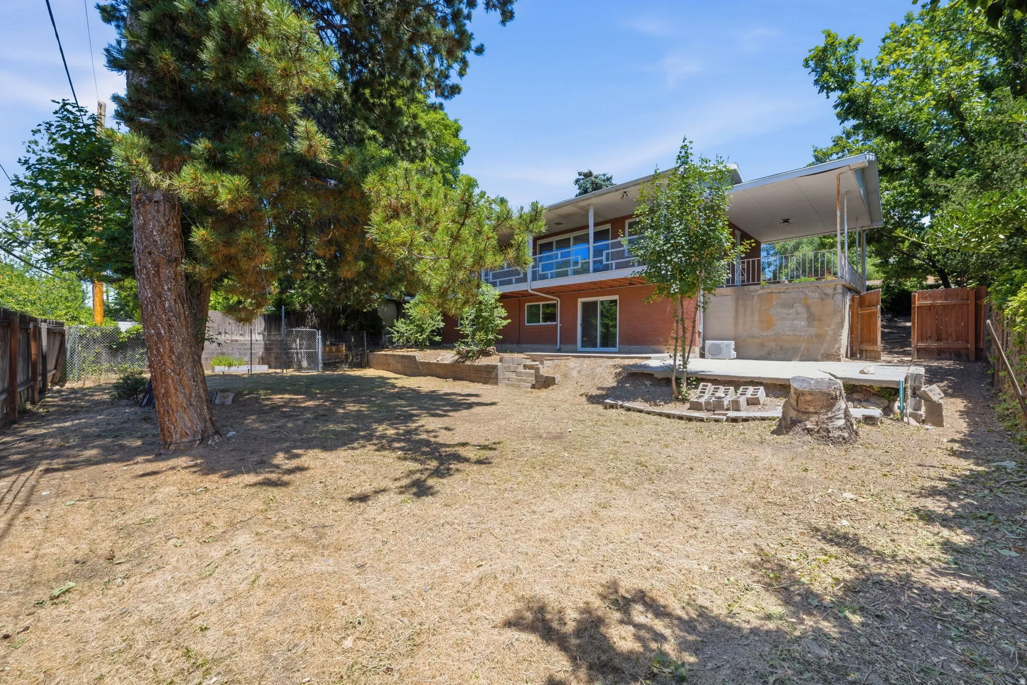 Expansive backyard featuring mature trees, a concrete patio, a concrete retaining wall, and a wood fence