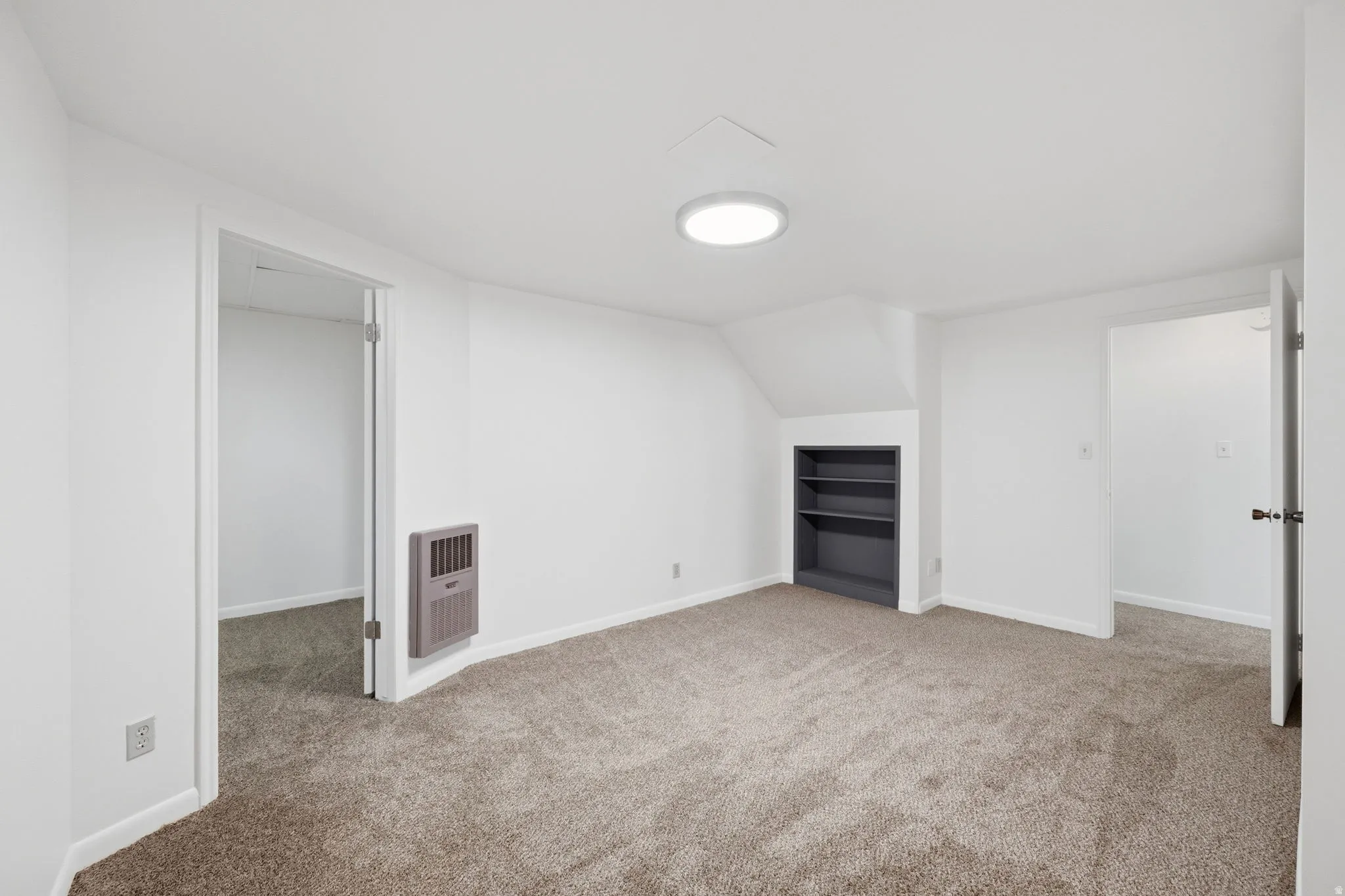 Carpeted room featuring a built-in bookshelf, wall-mounted heater, and recessed ceiling lighting