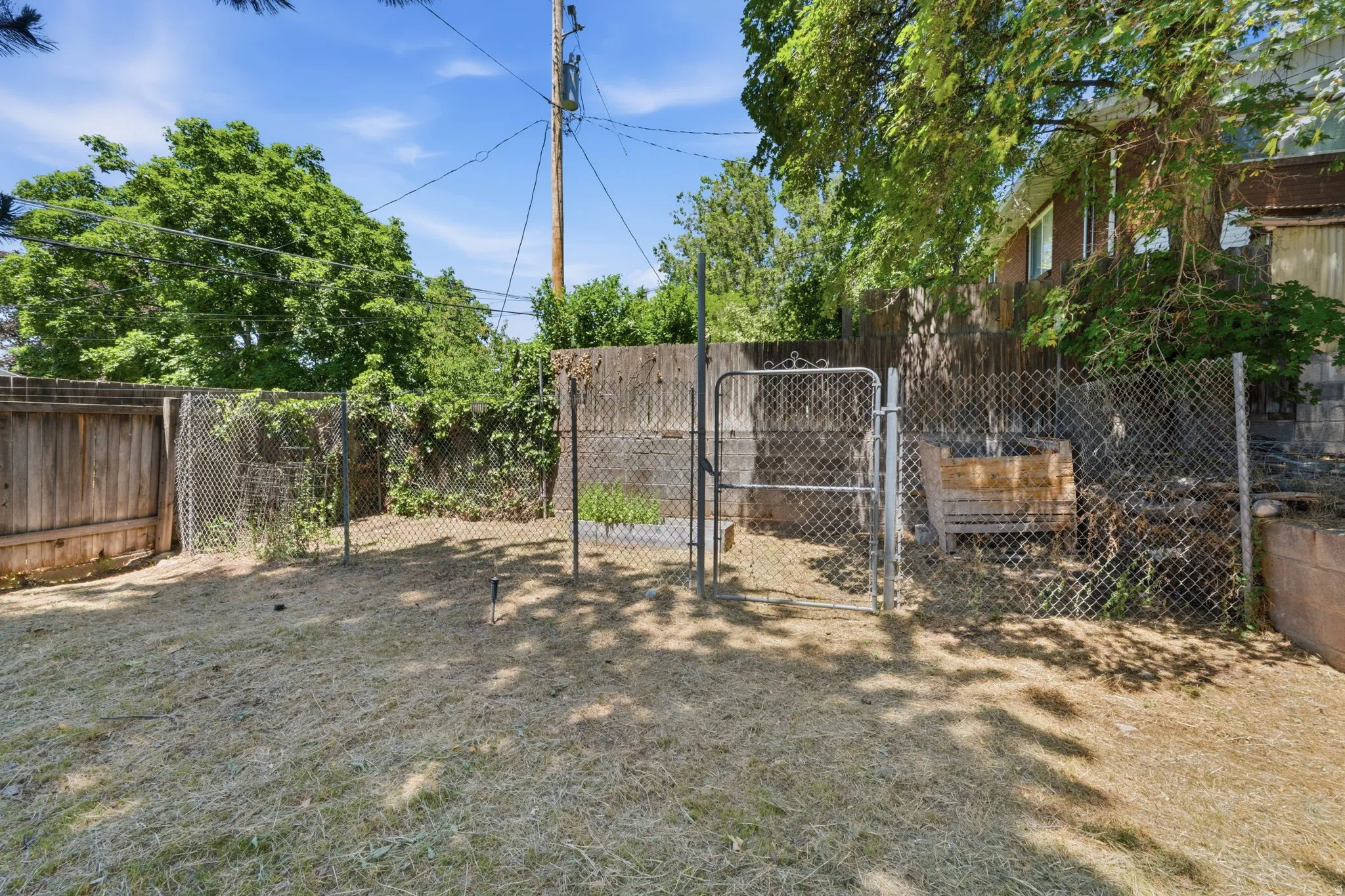 Expansive fenced backyard featuring a chain-link gate, wood privacy fencing, and mature trees