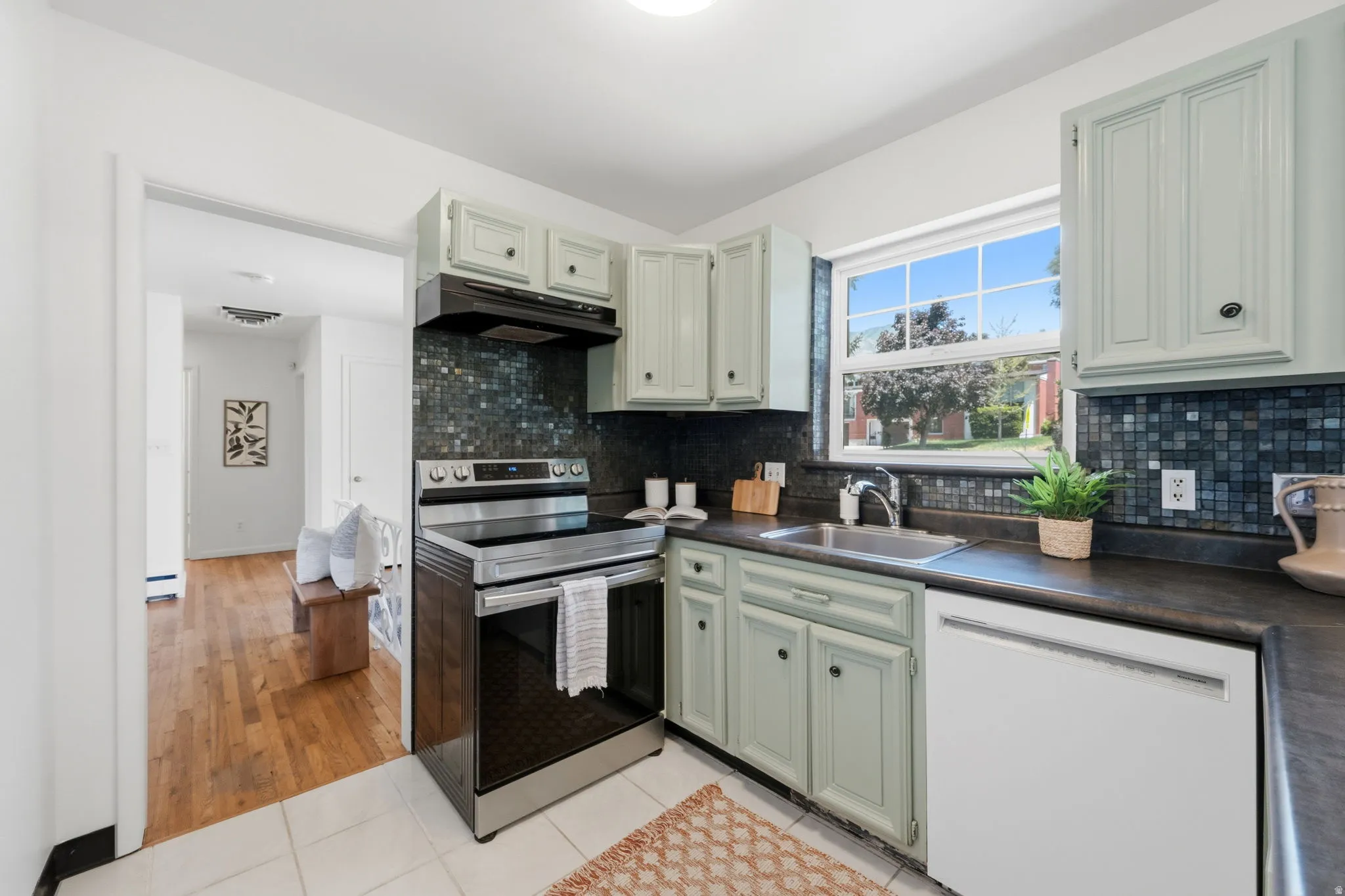 Kitchen with light green cabinetry, a mosaic tile backsplash, black countertops, and a stainless steel oven