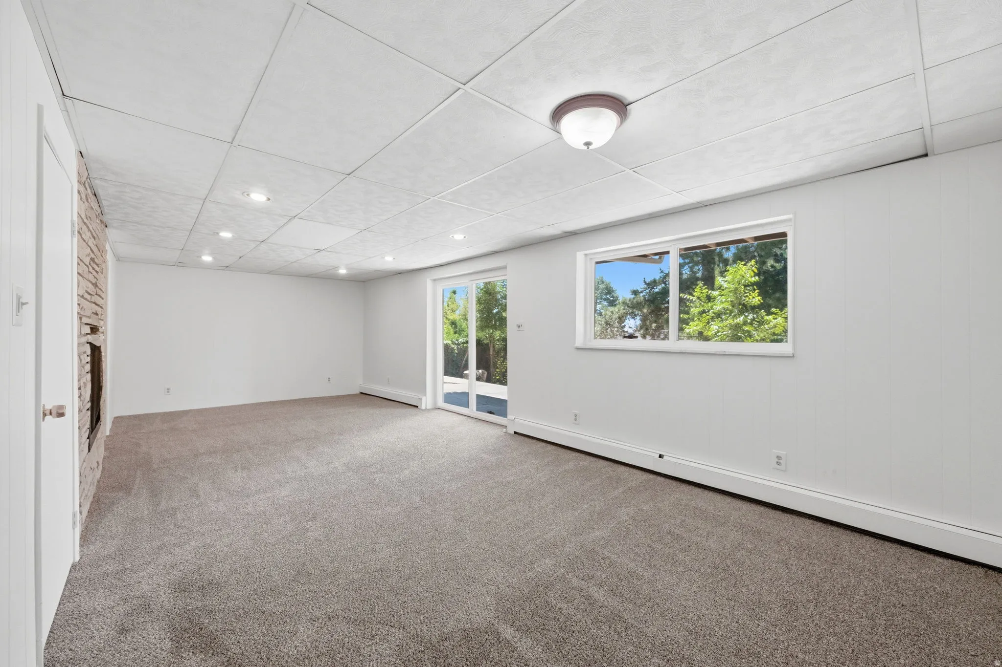 Spacious room featuring neutral carpeting, a drop ceiling with recessed lighting, and a stone-front fireplace