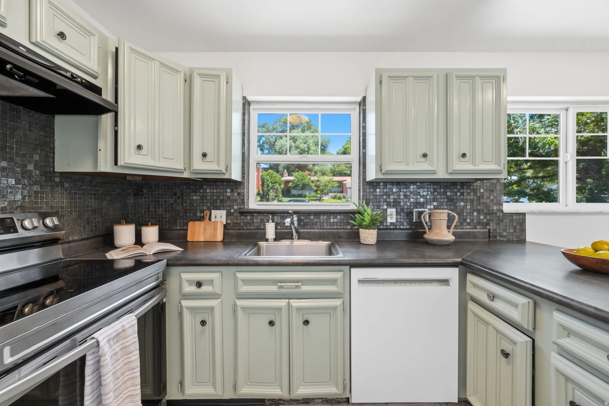 Kitchen featuring light-toned cabinetry with dark hardware, dark stone-look countertops, and a full-height mosaic tile backsplash