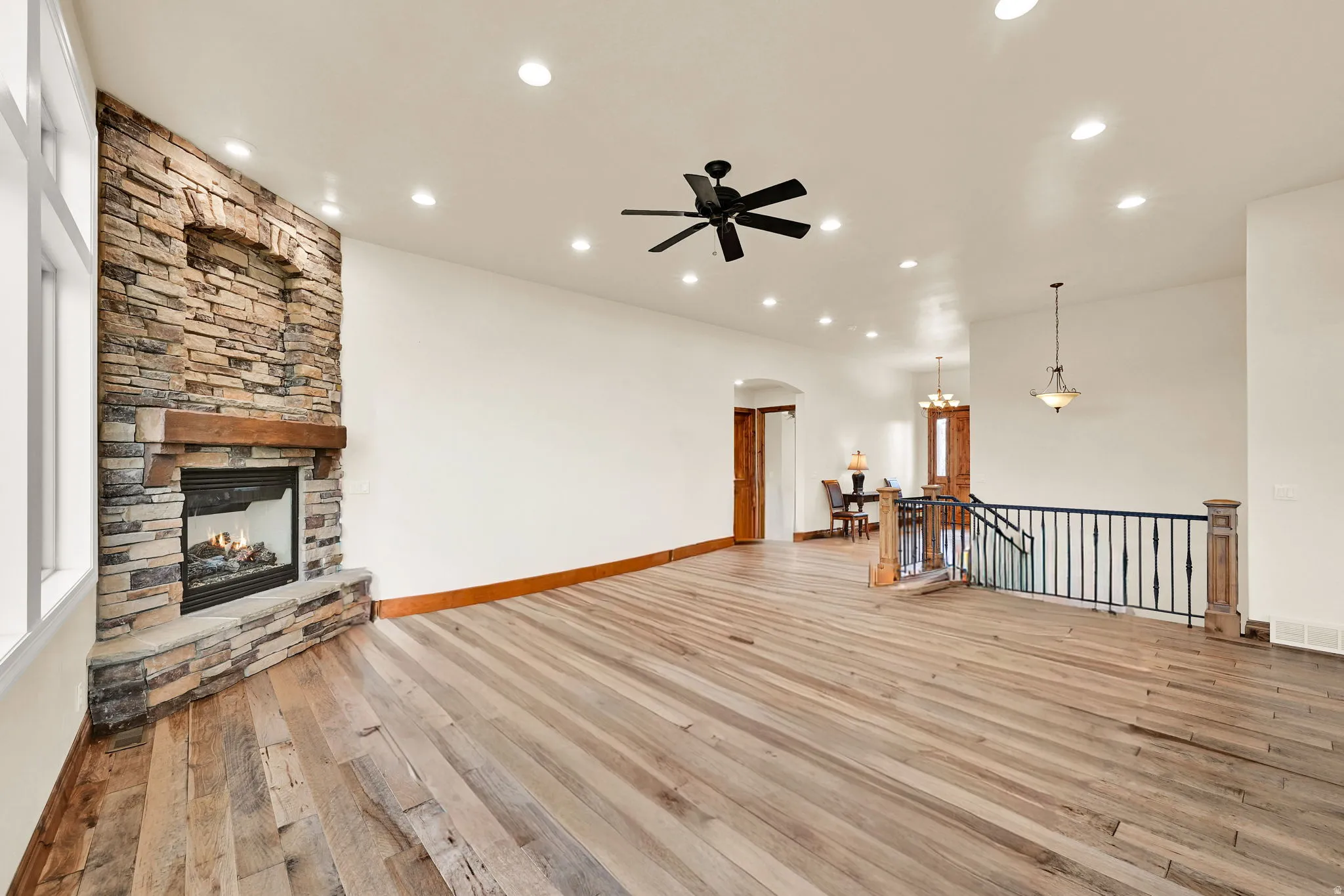 Spacious living area featuring a floor-to-ceiling stone fireplace with a wood mantel, wide plank wood-finish flooring, recessed lighting, and a ceiling fan