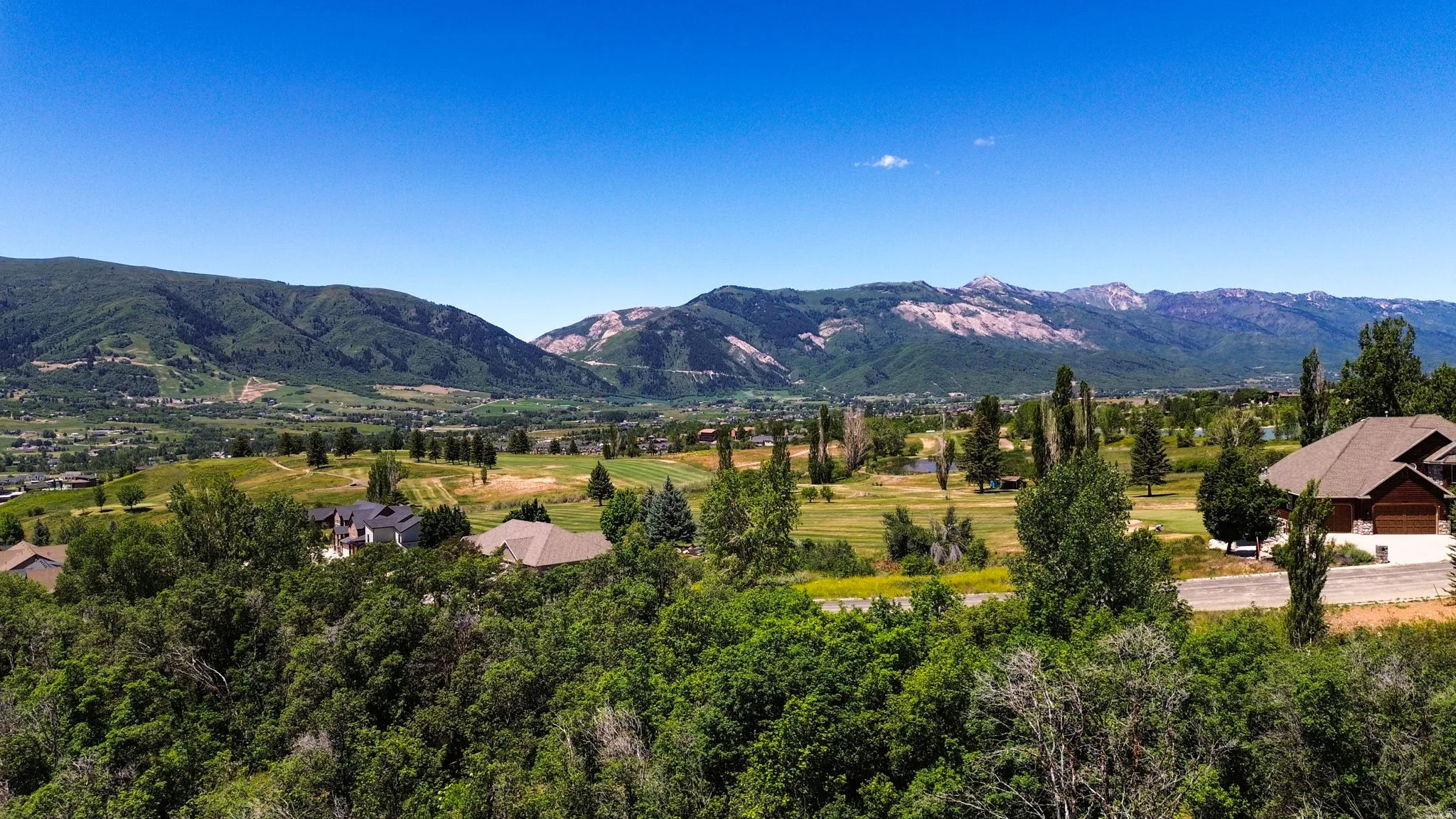 Expansive mountain landscape featuring a vibrant green valley, mature trees, and residential properties