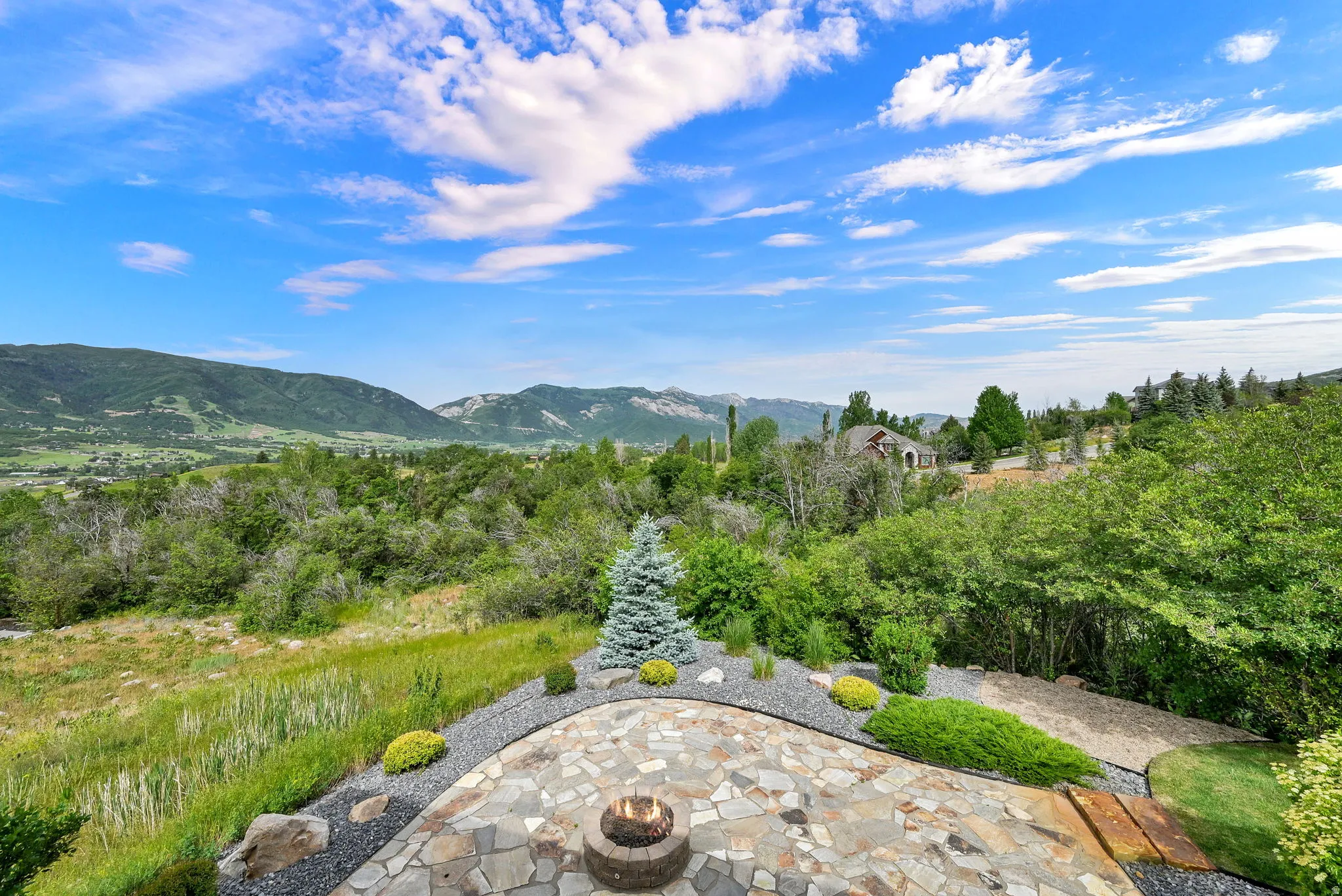 Stone patio with a built-in fire pit, surrounded by landscaped gravel beds and mature greenery