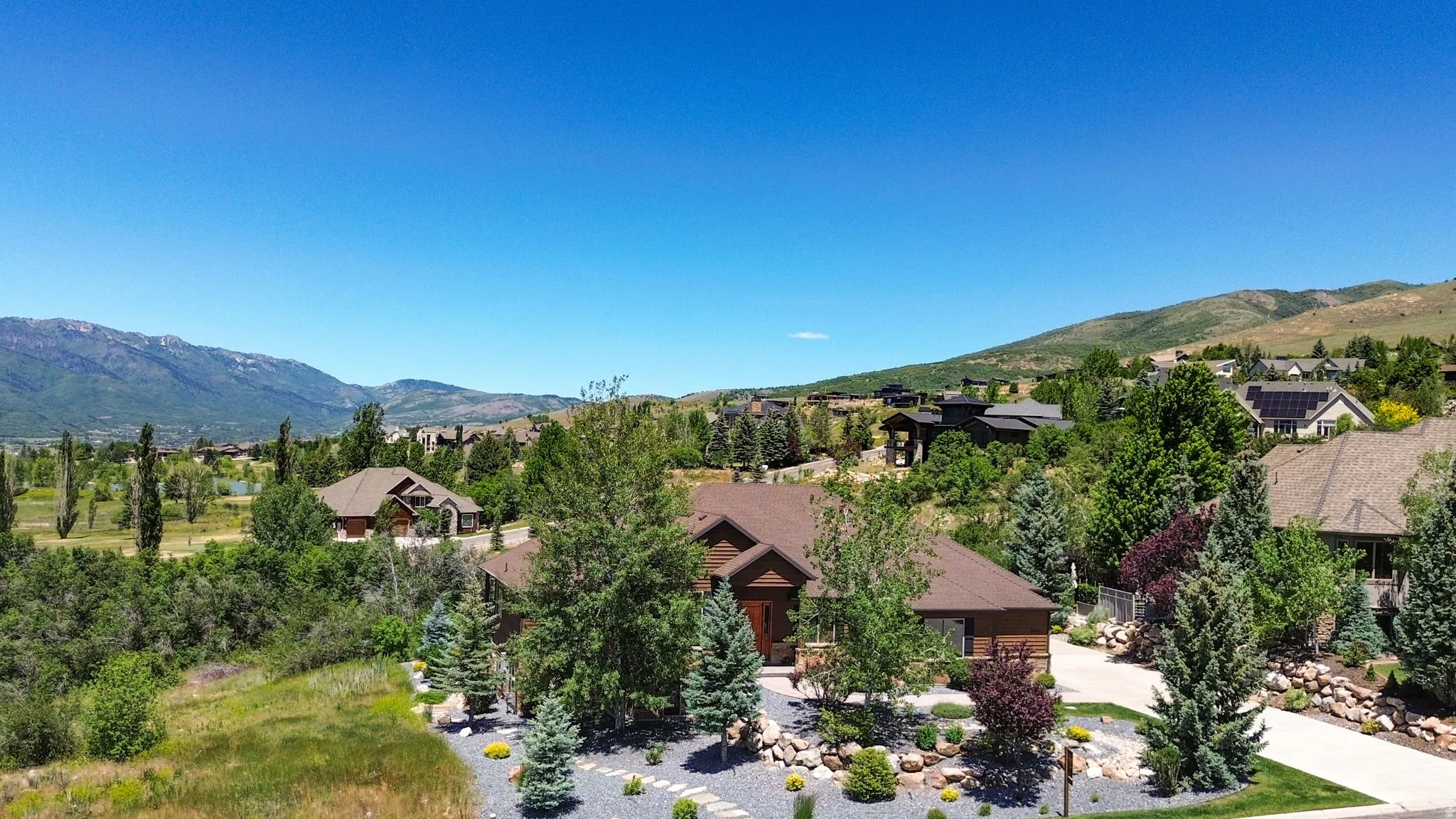 Spacious property featuring a brown exterior with stone accents, a landscaped front yard with stepping stones, a paved driveway, and mature trees and shrubs