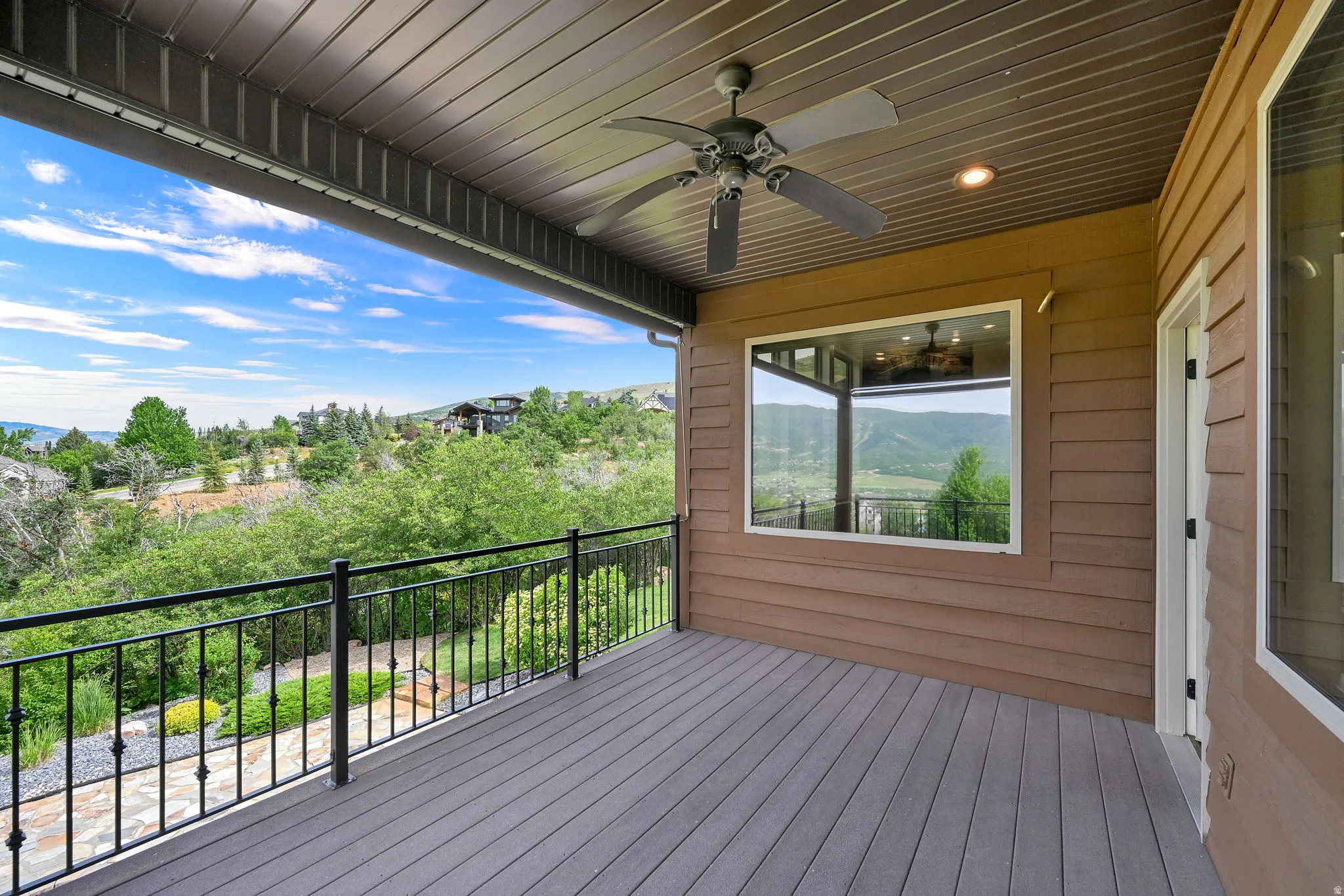 Expansive outdoor deck featuring wood-finish flooring, black metal railing, and a ceiling fan