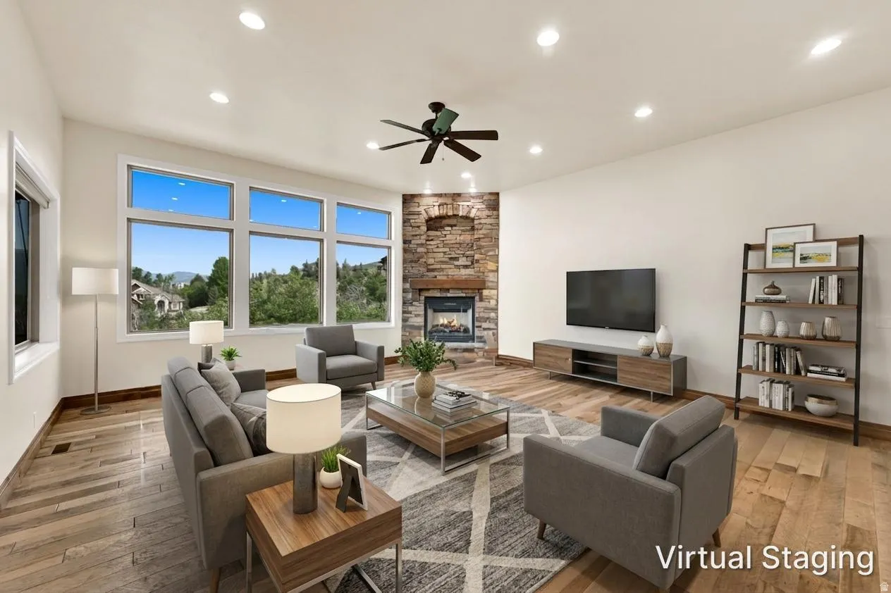 Spacious living area featuring large windows, wood-finish flooring, recessed lighting, and a stone-clad fireplace with a wood mantle