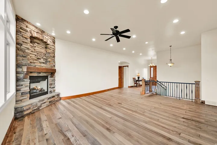 Spacious living area featuring a floor-to-ceiling stone fireplace with a wood mantel, wide plank wood-finish flooring, recessed lighting, and a ceiling fan