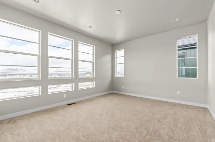Spacious room featuring multiple large windows, recessed lighting, neutral wall paint, white baseboards, and light-colored carpet