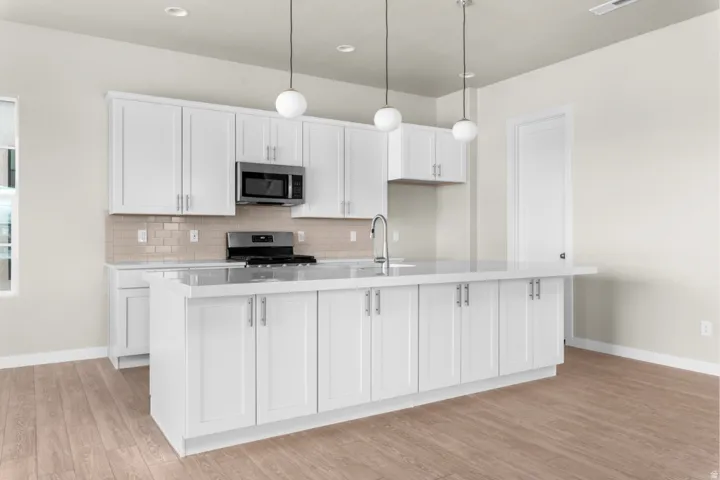 Modern kitchen featuring white shaker cabinetry, stainless steel appliances, a light-toned tile backsplash, and a central island with an integrated sink and pendant lighting
