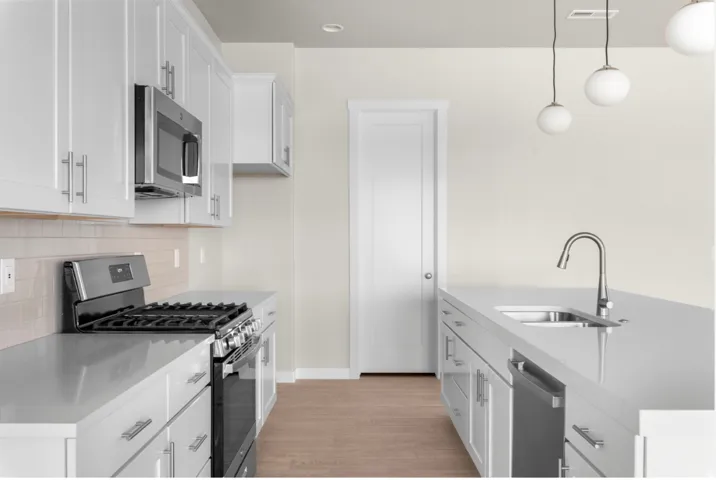 Contemporary kitchen featuring white shaker cabinetry, stainless steel appliances, a center island with sink, pendant lighting, and wood-finish flooring