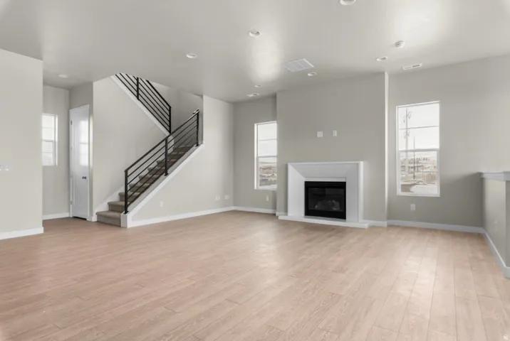 Open-concept interior featuring wood-finish flooring, a contemporary fireplace with a white mantel, and a staircase with dark metal railings