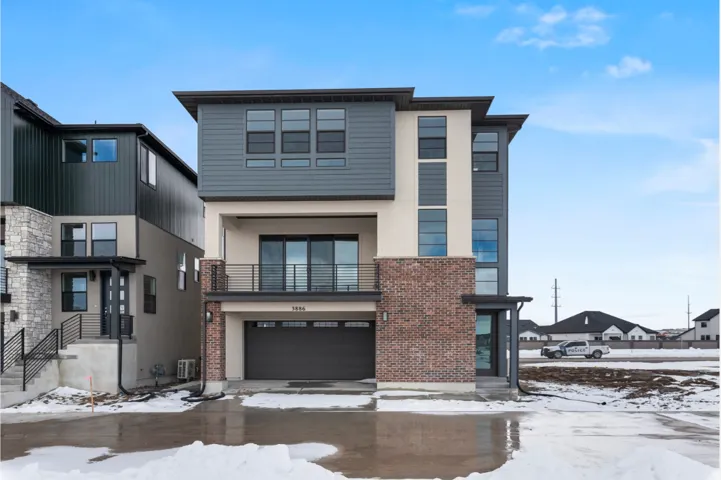 Contemporary multi-story facade featuring mixed-material construction, a second-story balcony with metal railing, an integrated garage, and a prominent front entry with a dark-frame glass door