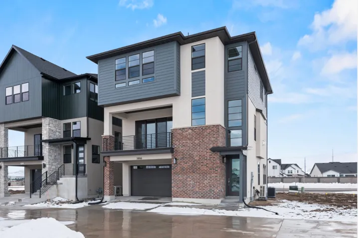 Contemporary multi-level residence featuring brick accents, horizontal siding, vertical paneling, a single-car garage, and a second-story balcony with metal railings