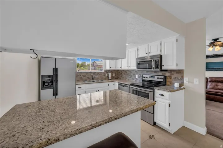Kitchen featuring granite countertops, white cabinetry, stainless steel appliances, a tile backsplash, and a window above the sink