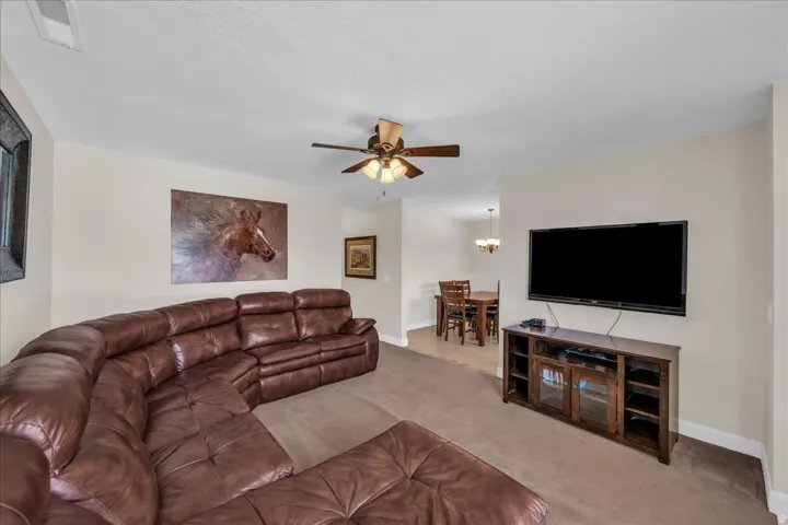 Open-concept living area featuring a ceiling fan with integrated lighting, carpeted flooring, and neutral wall tones