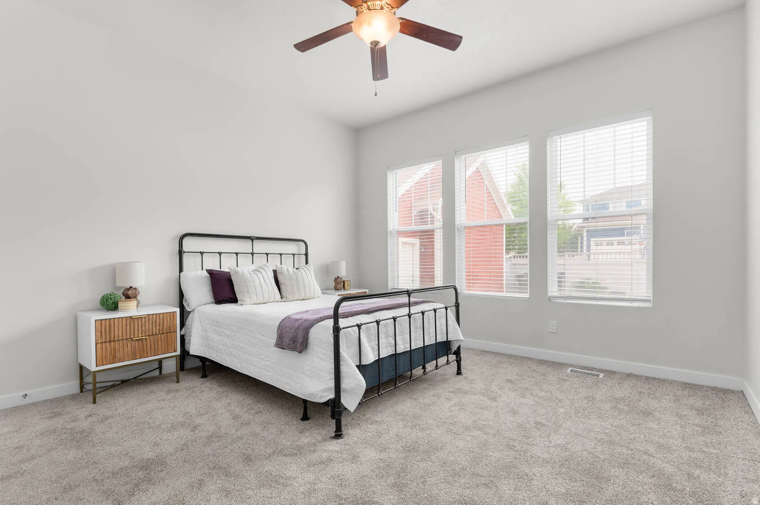 Bright bedroom featuring three large windows, textured carpeting, a ceiling fan, and painted walls