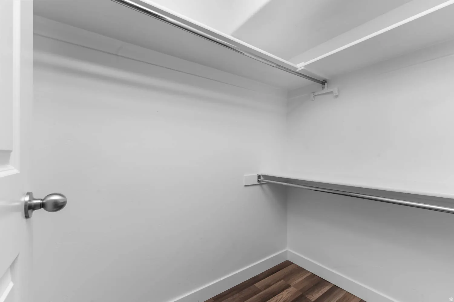 Interior closet featuring white walls, wood-finish flooring, multiple shelving units, and chrome hanging rods