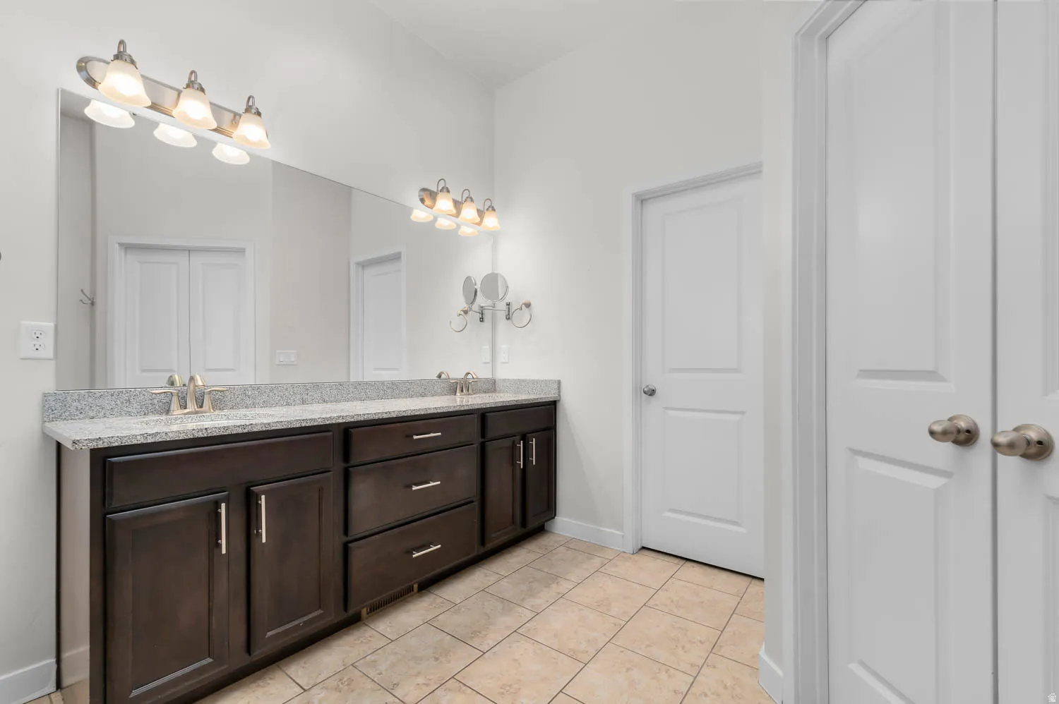 Double vanity featuring a light granite-style countertop, undermount sinks, and ample dark wood cabinetry