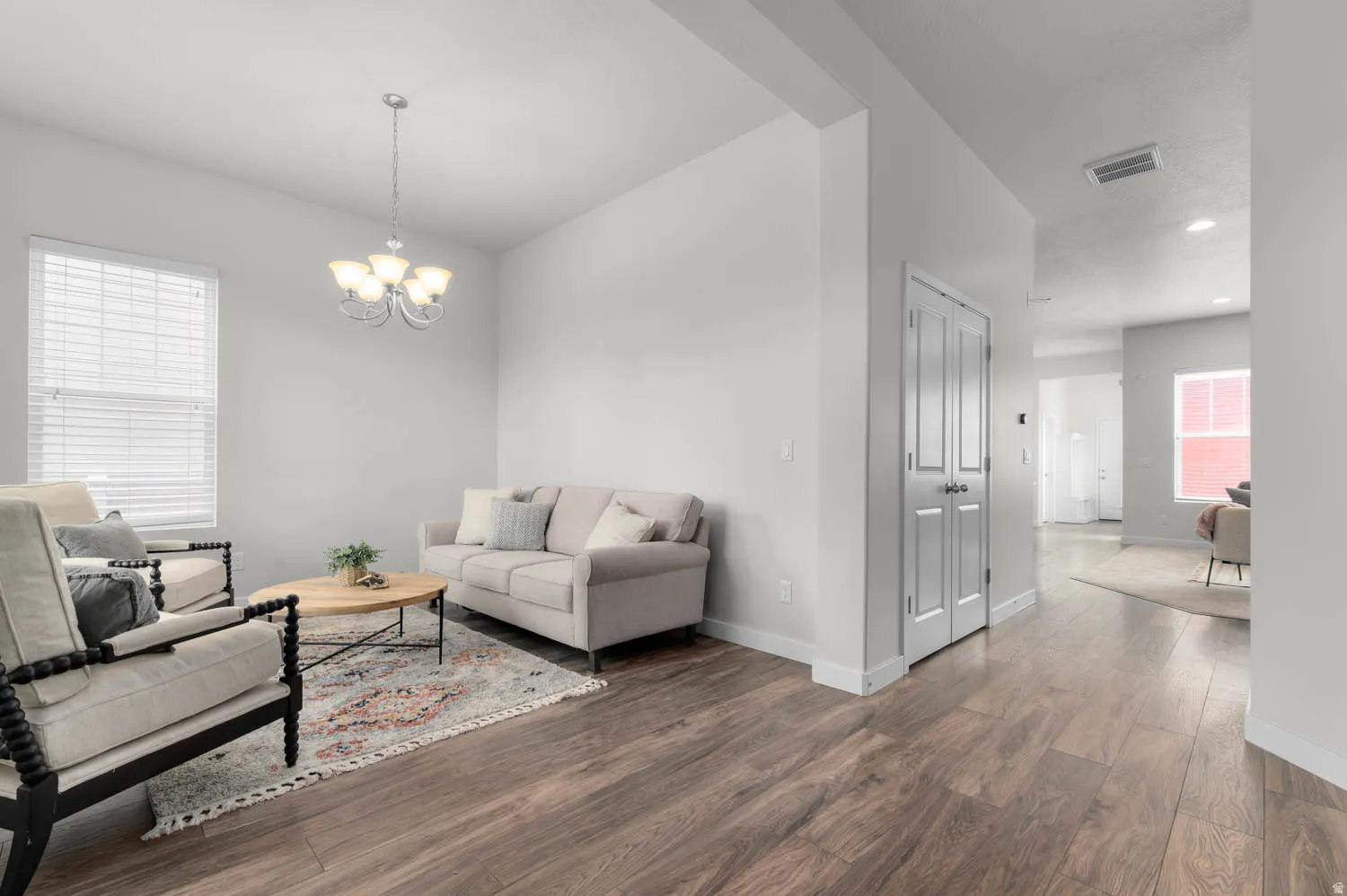 Spacious living area featuring wood-finish flooring, light gray walls, white trim, and a five-light chandelier
