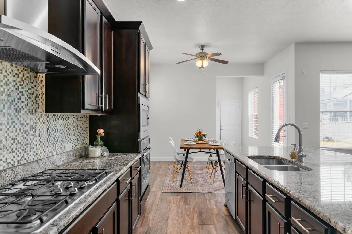 Kitchen featuring dark wood-finish cabinetry, granite countertops, a mosaic tile backsplash, stainless steel appliances, and wood-finish flooring