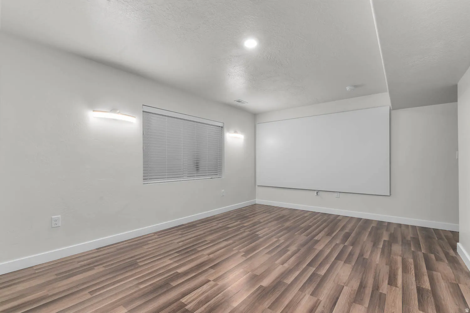 Spacious room featuring wood-finish flooring, recessed ceiling lighting, and a window with horizontal blinds