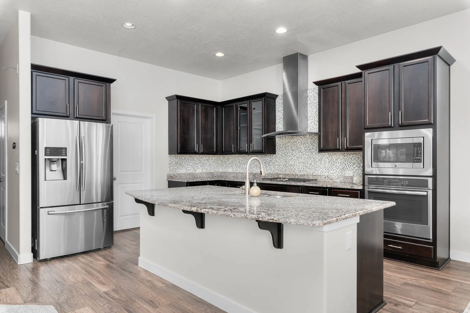 Kitchen featuring a central island with granite countertop, dark wood cabinetry, stainless steel appliances, a mosaic tile backsplash, and wood-finish flooring