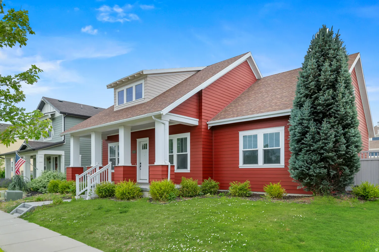 Red siding exterior featuring white trim accents, a front porch with white columns, a dormer window, and a light brown shingle roof