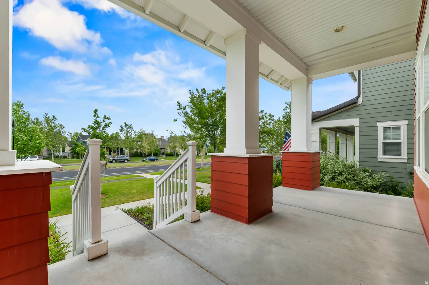 Covered front porch featuring a concrete surface, white painted railings, white columns, and red siding accents