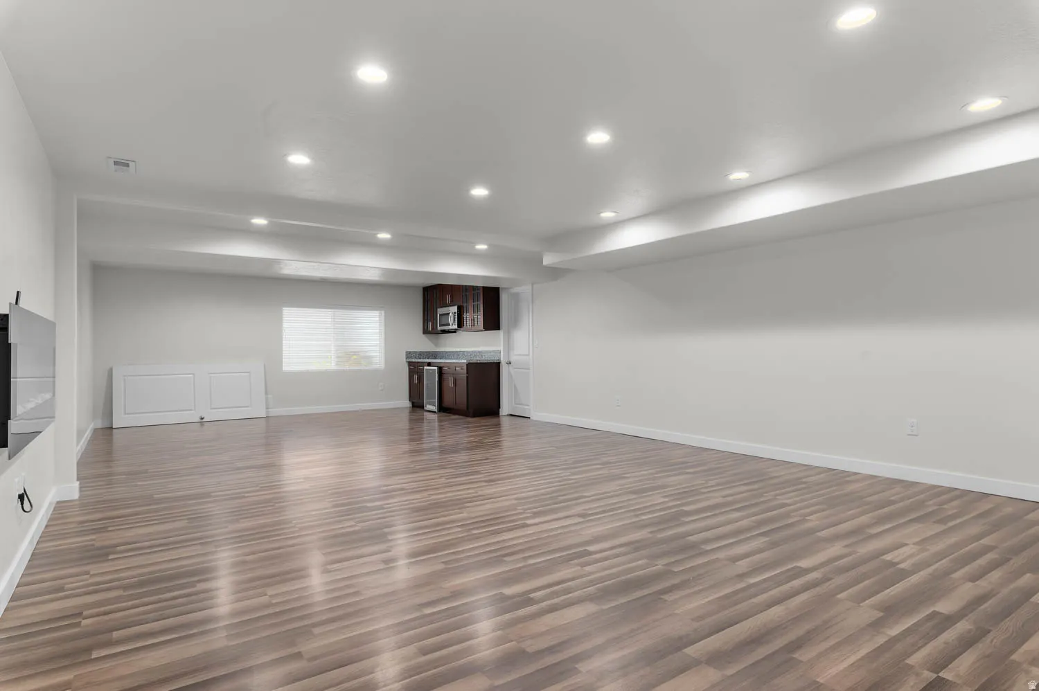 Spacious entertainment area featuring wood-finish flooring, recessed lighting, and a built-in wet bar with dark wood cabinetry
