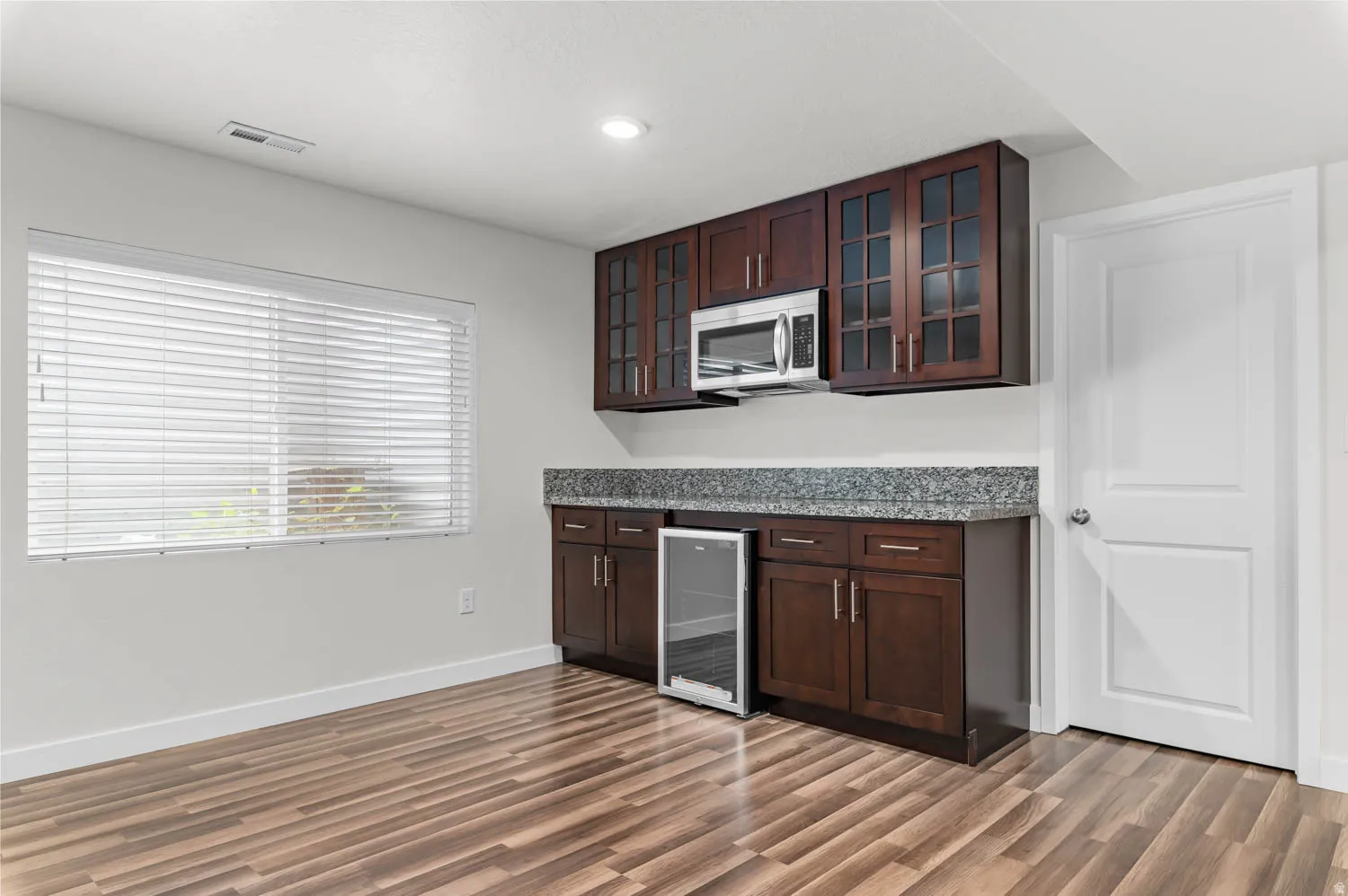 Integrated wet bar featuring dark wood-finish cabinetry, a granite-patterned countertop, and a built-in beverage cooler