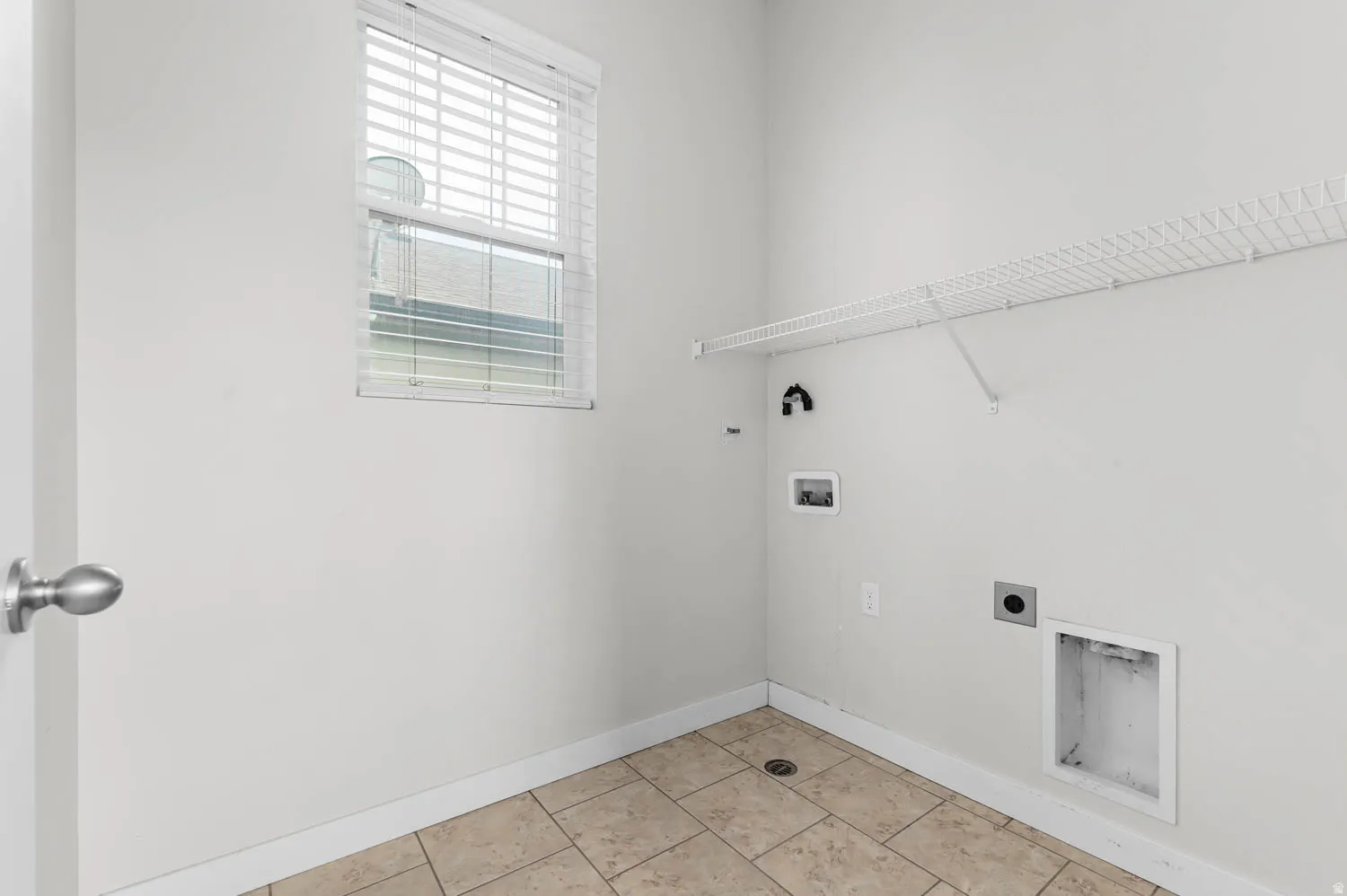 Utility room featuring tile flooring, a window with blinds, and a wire storage shelf