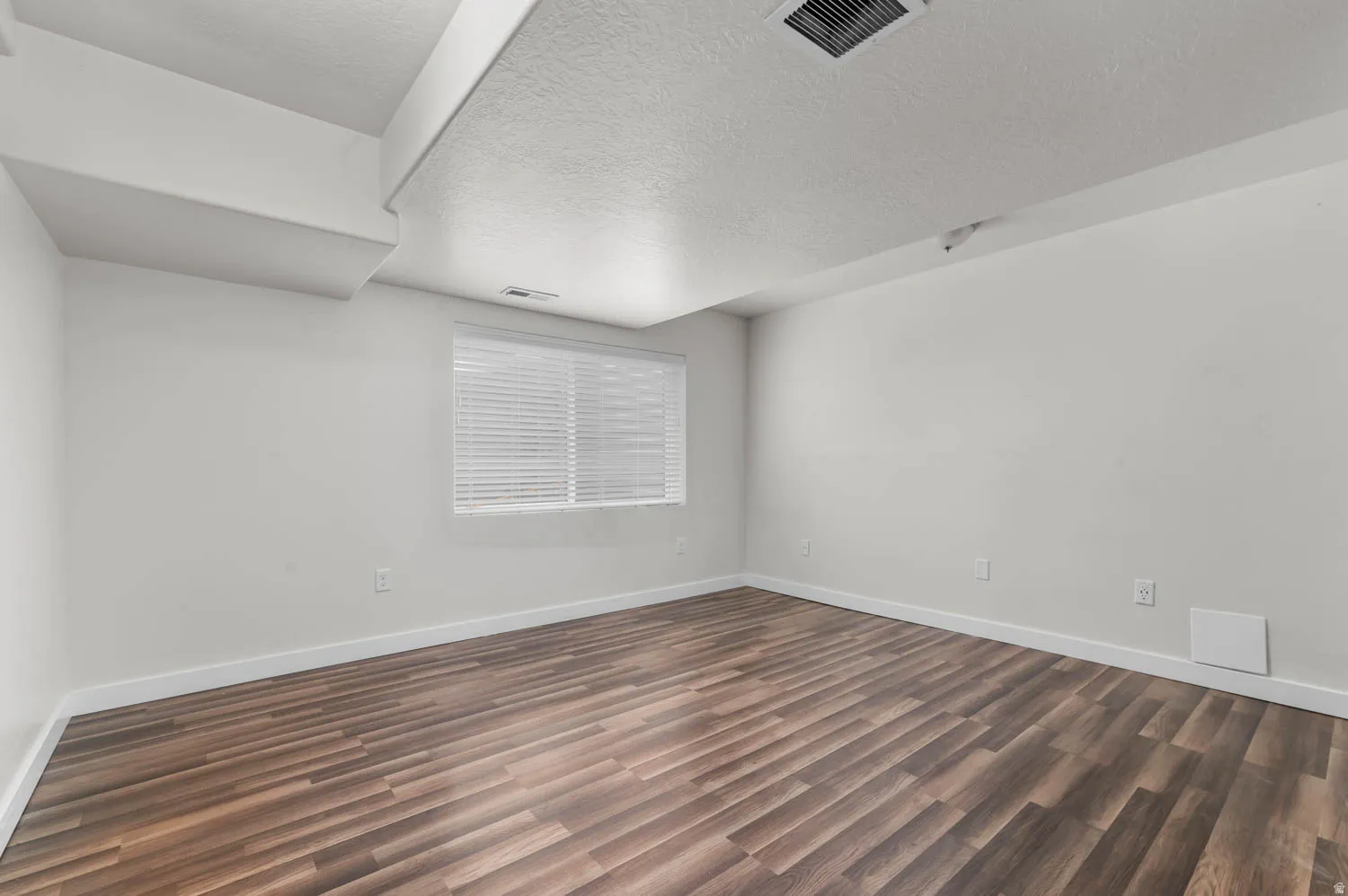 Room featuring wood-finish flooring, white walls, white trim, and a window with blinds