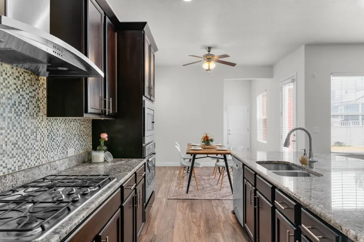 Kitchen featuring dark wood-finish cabinetry, granite countertops, a mosaic tile backsplash, stainless steel appliances, and wood-finish flooring