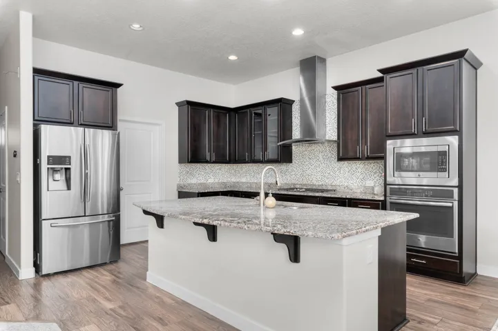 Kitchen featuring a central island with granite countertop, dark wood cabinetry, stainless steel appliances, a mosaic tile backsplash, and wood-finish flooring