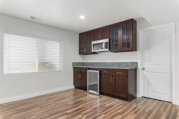Integrated wet bar featuring dark wood-finish cabinetry, a granite-patterned countertop, and a built-in beverage cooler