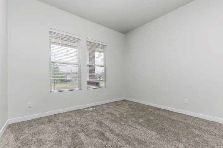 Room with two windows featuring horizontal blinds, light gray textured carpeting, white baseboards, and neutral wall paint