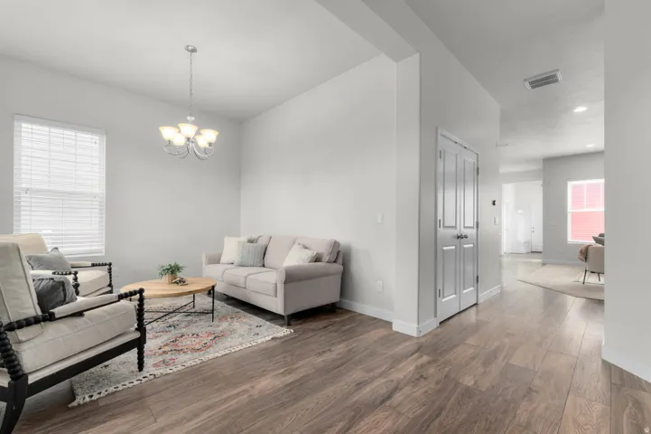 Spacious living area featuring wood-finish flooring, light gray walls, white trim, and a five-light chandelier