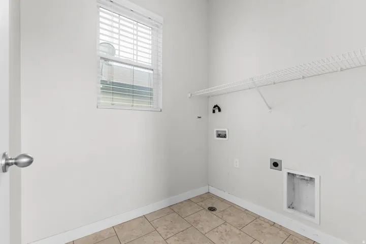 Utility room featuring tile flooring, a window with blinds, and a wire storage shelf