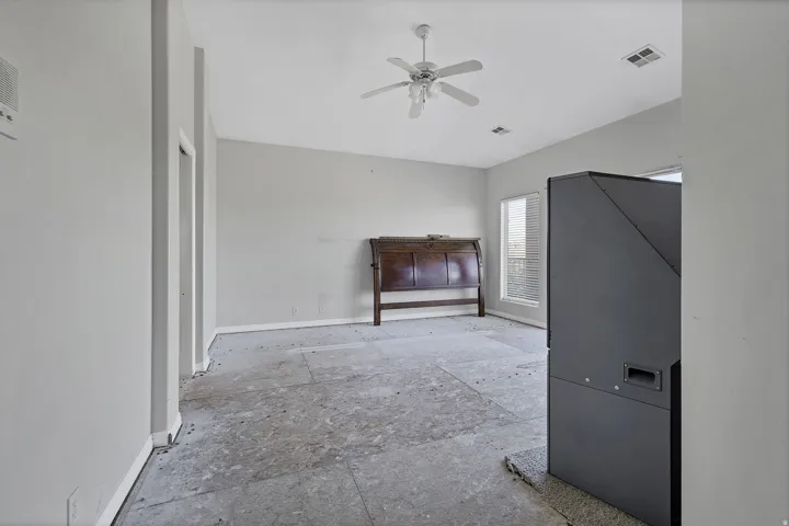 Spacious room featuring neutral painted walls, multiple windows, a ceiling fan with integrated lighting, and a built-in dark gray cabinet