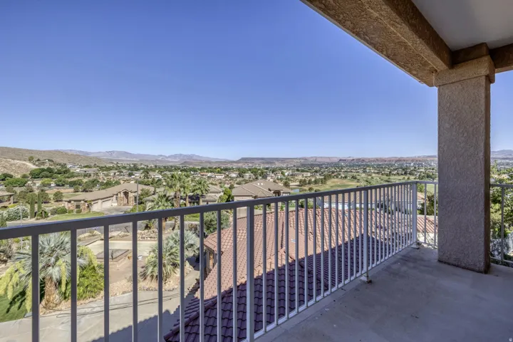Expansive concrete balcony featuring a white metal railing, textured stucco columns, and a tile roofline below