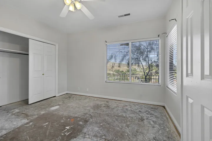 Spacious room featuring multiple windows with horizontal blinds, a ceiling fan with integrated lighting, and a closet with bifold doors