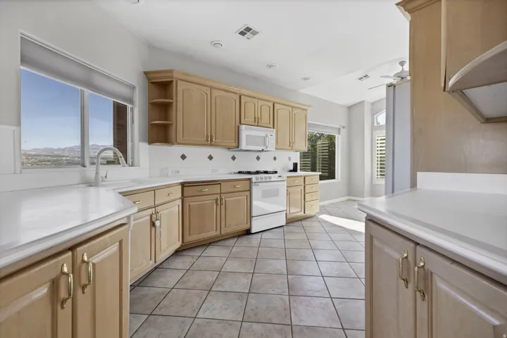 Kitchen featuring light wood cabinetry, white countertops, a white built-in microwave, and a white range