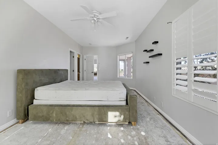 Vaulted ceiling bedroom with white plantation shutters, a ceiling fan, and light gray walls