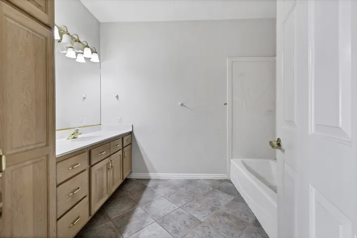Bathroom vanity featuring a light-toned wood-finish cabinet with brass hardware, a white countertop, and an integrated sink with a brass faucet